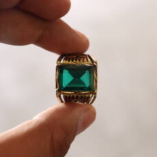 An Ancient Golden Ring embedded with Green Emerald Stone Gem held by a person in between fingers